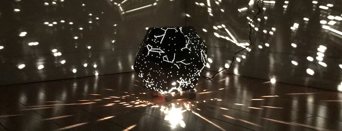 A completed star projector sitting in the corner of a room projecting stars and constellations onto nearby walls